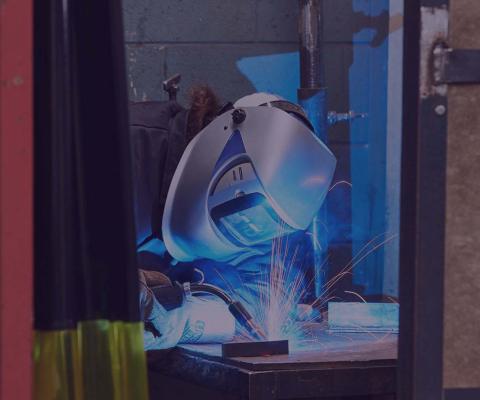 Welder wearing welding mask, welding a piece of steel